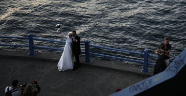 A groom and a bride pose for a photo session at Galata Bridge in Istanbul, Türkiye, July 24, 2023. (AP Photo)