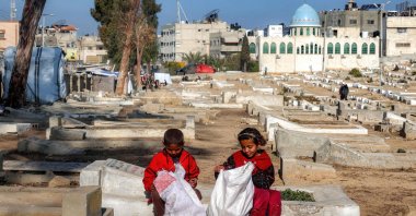 Two children sit by graves at a cemetery where families displaced by Israel&#039;s attacks are taking shelter, Deir el-Balah, central Gaza Strip, Palestine, Jan. 12, 2025. (AFP Photo)