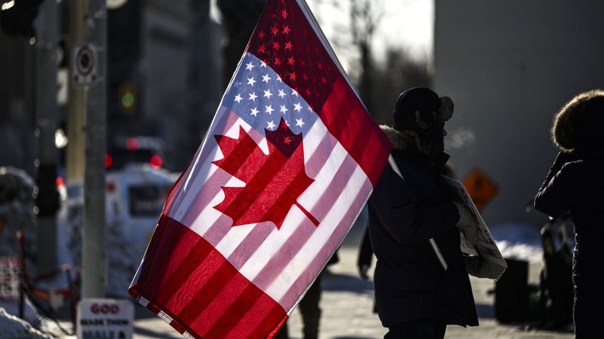 A protester holds the flags of Canada and the United States outside on Parliament Hill, Ottawa, Canada, Feb. 1, 2025. (The Canadian Press via AP)