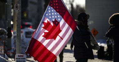 A protester holds the flags of Canada and the United States outside on Parliament Hill, Ottawa, Canada, Feb. 1, 2025. (The Canadian Press via AP)
