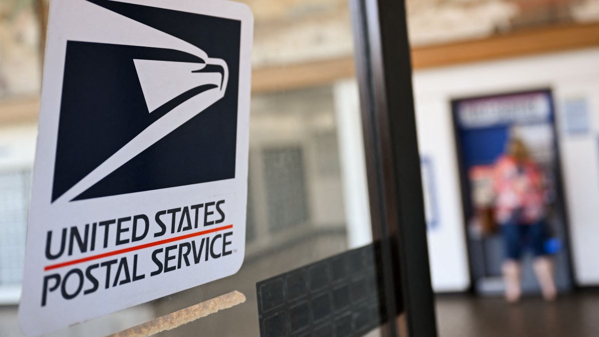 The United States Postal Service (USPS) logo is displayed on a door as a postal customer uses a self-service mail shipping kiosk to ship a package at a USPS post office in Redondo Beach, California, U.S., Aug. 28, 2024. (AFP Photo)