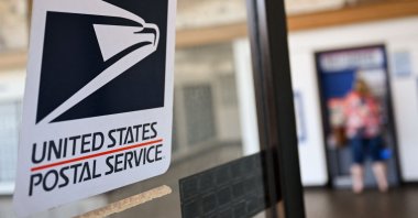 The United States Postal Service (USPS) logo is displayed on a door as a postal customer uses a self-service mail shipping kiosk to ship a package at a USPS post office in Redondo Beach, California, U.S., Aug. 28, 2024. (AFP Photo)