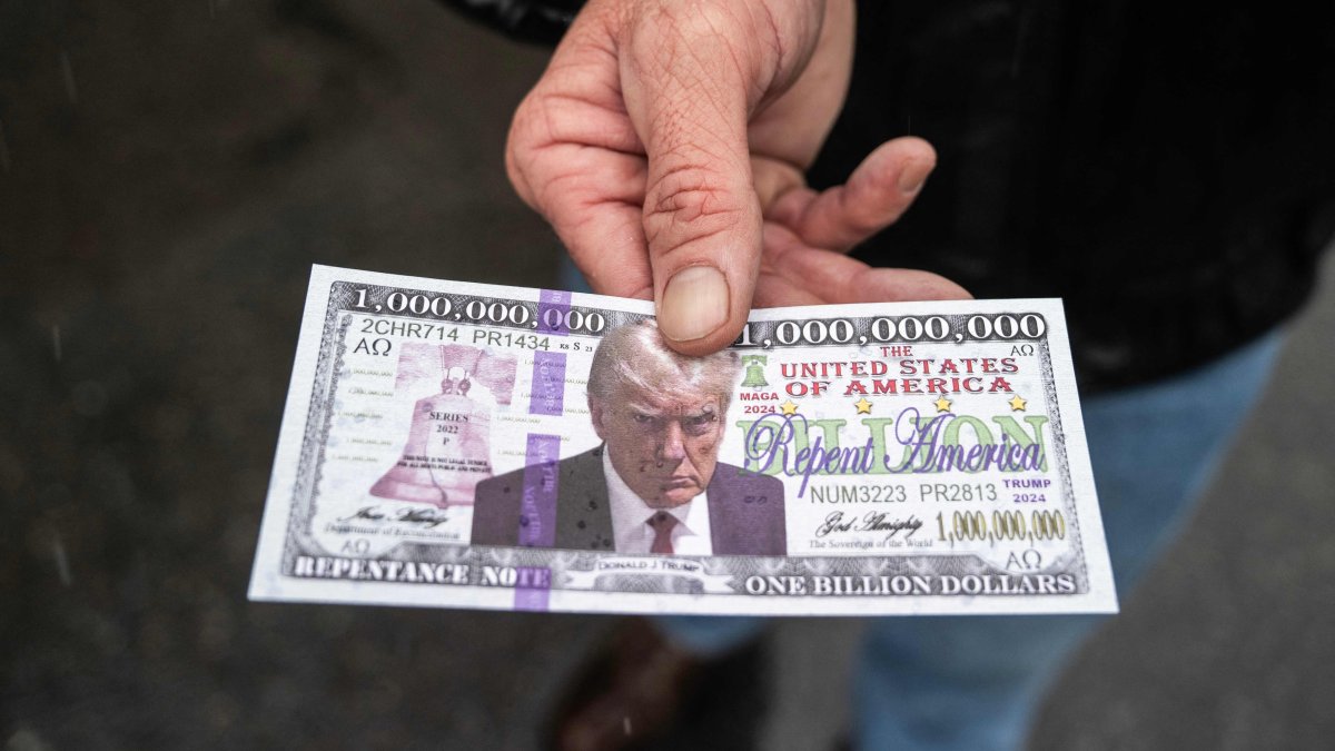 A man holds out a fake &quot;Trump bill&quot; with Bible verses on the back that he is handing out to supporters of U.S. President-elect Donald Trump lining up on the National Mall for a MAGA victory rally at Capital One Arena, one day ahead of Trump&#039;s inauguration, Washington, DC, U.S., Jan. 19, 2025,  (AFP Photo)