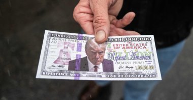 A man holds out a fake &quot;Trump bill&quot; with Bible verses on the back that he is handing out to supporters of U.S. President-elect Donald Trump lining up on the National Mall for a MAGA victory rally at Capital One Arena, one day ahead of Trump&#039;s inauguration, Washington, DC, U.S., Jan. 19, 2025,  (AFP Photo)
