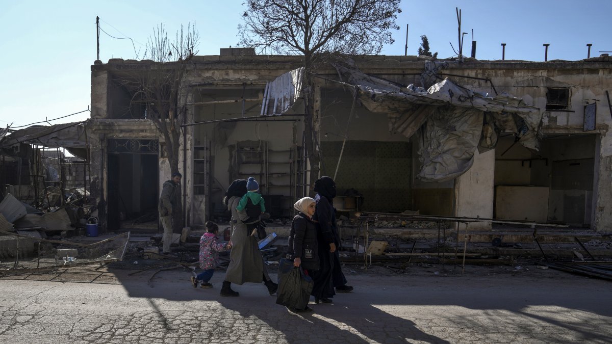 A family walks past destroyed shops in Tal Rifaat, Syria, Jan. 28, 2025. (AP Photo)