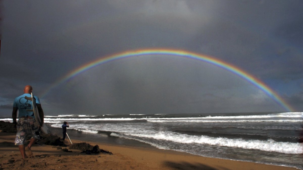 Professional surfers make their way to the water while a large rainbow crosses the ocean during the Pro Hawaii surfing contest at Ali&#039;i Beach, Haleiwa, Hawaii, U.S., Nov. 18, 2005. (AP Photo)