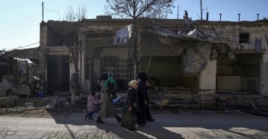 A family walks past destroyed shops in Tal Rifaat, Syria, Jan. 28, 2025. (AP Photo)