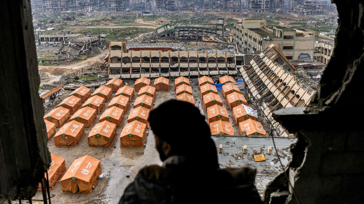 A man standing atop a heavily damaged building looks out to view tents sheltering displaced Palestinians erected in the yard of a secondary school, northern Gaza City, Palestine, Feb.10, 2025. (AFP Photo)