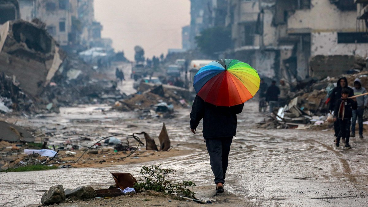 A man walks with an umbrella along a muddied street past the rubble of destroyed and heavily-damaged buildings, Gaza City, Palestine, Feb. 10, 2025. (AFP Photo)