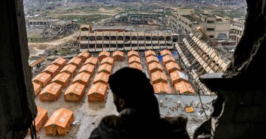A man standing atop a heavily damaged building looks out to view tents sheltering displaced Palestinians erected in the yard of a secondary school, northern Gaza City, Palestine, Feb.10, 2025. (AFP Photo)