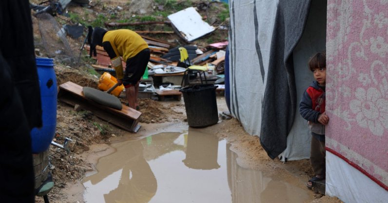 A Palestinian child stands at the entrance of a tent as a man clears the mud during the rainy season in Beit Hanoun in the northern Gaza Strip on Feb. 12, 2025. (AFP Photo)