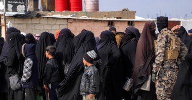 A U.S.-backed PKK/YPG terrorist passes in front of women and children queueing at the al-Hol camp, northeastern Hassakeh province, Syria, Feb. 9, 2025. (AFP Photo)