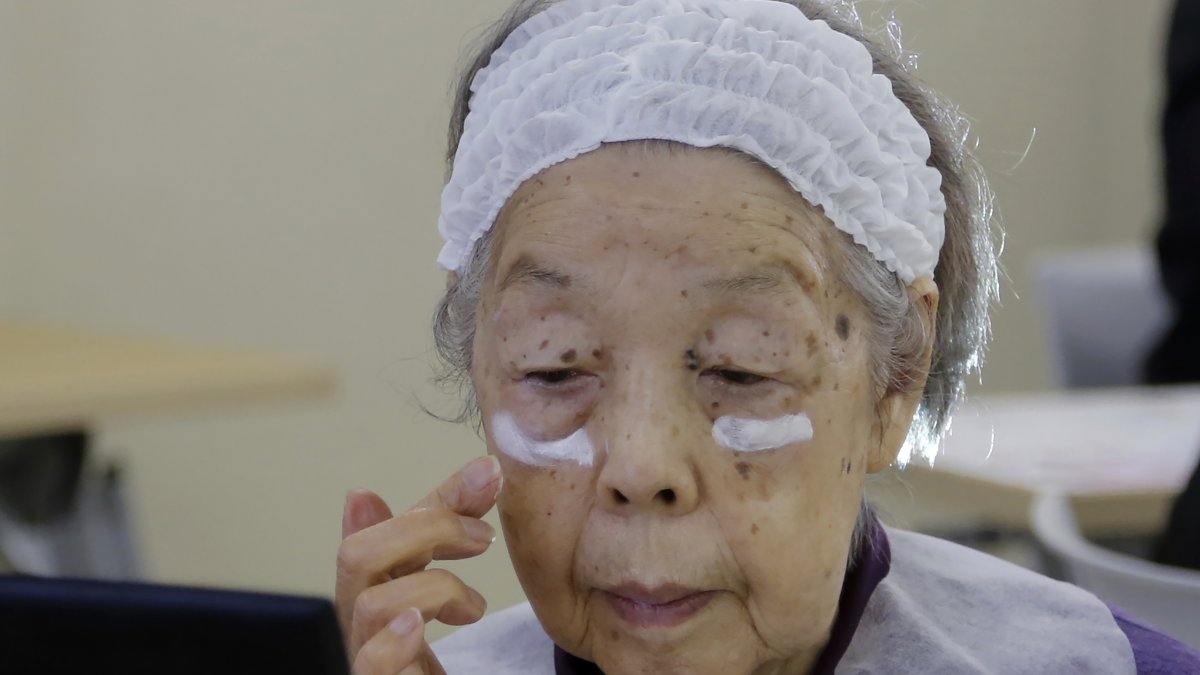 Yoshiko Abe tries on cream at a class for the elderly at a Tokyo housing complex that teaches people to stay healthy and beautiful through makeup, Tokyo, Japan, Feb. 14, 2025. (AP Photo)