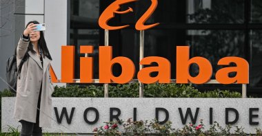 A woman poses for a selfie next to signage for e-commerce giant Alibaba, Xuhui district, Shanghai, China, Feb. 22, 2025. (AFP Photo)