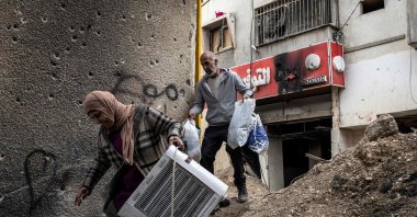 Displaced Palestinians carry personal belongings they retrieved from their home as they walk past a bullet-riddled wall in the Jenin camp for refugees, occupied West Bank, Palestine, Feb. 24, 2025. (AFP Photo)