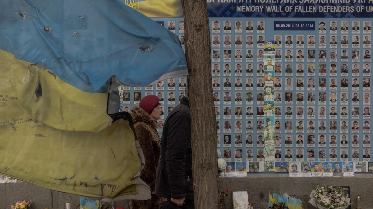 People visit the "Wall of Remembrance of the Fallen for Ukraine," a memorial for fallen Ukrainian soldiers right next to a battered Ukrainian flag, downtown Kyiv, Ukraine, March 4, 2025. (AFP Photo)