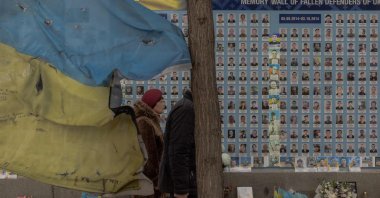 People visit the "Wall of Remembrance of the Fallen for Ukraine," a memorial for fallen Ukrainian soldiers right next to a battered Ukrainian flag, downtown Kyiv, Ukraine, March 4, 2025. (AFP Photo)