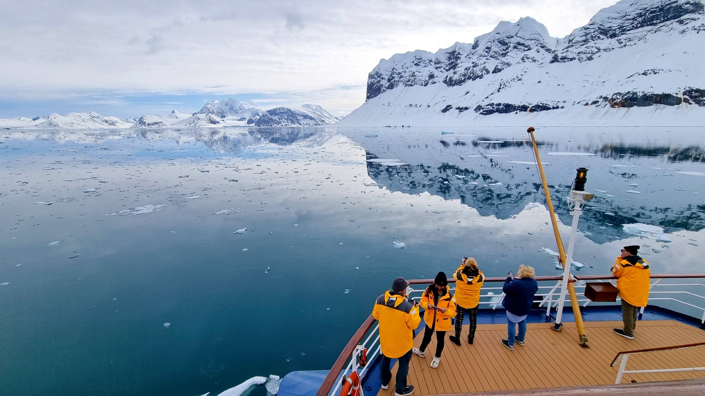 Tourists admire snow-covered Arctic reflections from the expedition ship&#039;s stern, Svalbard, Norway, June 3, 2023. (Shutterstock Photo})