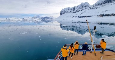 Tourists admire snow-covered Arctic reflections from the expedition ship&#039;s stern, Svalbard, Norway, June 3, 2023. (Shutterstock Photo})