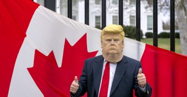 A visitor to the city wearing a mask of President Donald Trump poses for a photo in front of a Canadian flag being held by tourists from Toronto showing their support for Canada regarding trade tariffs, in front of the White House, Washington, U.S., March 13, 2025. (AP Photo)