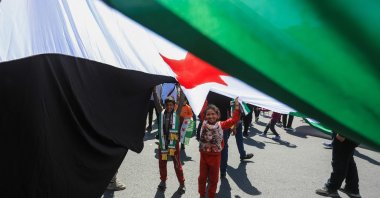 Children stand under a large national flag as they celebrate the 14th anniversary of the Syrian uprising, at a rally in Umayyad Square, Damascus, Syria, March 15, 2025. (AFP Photo)