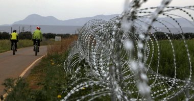 Two men cycle along a row of razor wire on the southern side of a U.N. buffer zone that cuts across the ethnically divided island of Cyprus, March 9, 2021. (AP Photo)