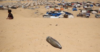 An unexploded shell lies on a sand dune as a young boy sits near a makeshift camp for displaced Palestinians in the area of Tel al-Sultan in Rafah in the southern Gaza Strip, Palestine, May 30, 2024. (AFP Photo)