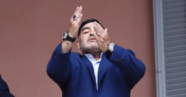 Diego Maradona gestures to fans next to a small, generic replica of a FIFA World Cup soccer trophy after he meets with Argentine President Alberto Fernandez, Buenos Aires, Argentina, Dec. 26, 2019. (AP Photo)