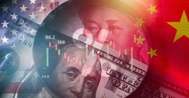 A magnifier glass focuses on a U.S. dollar and yuan banknote with U.S. and China flags in the background. (Shutterstock Photo)