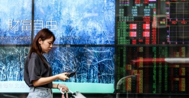 A woman walks past a screen showing share prices of the stock market, Taipei, Taiwan, April 10, 2025. (AFP Photo)