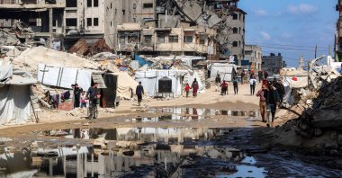 People walk past a puddle of water by tent shelters erected near the rubble of a collapsed building in the Nasr neighbourhood in western Gaza City, April 15, 2025. (AFP Photo)
