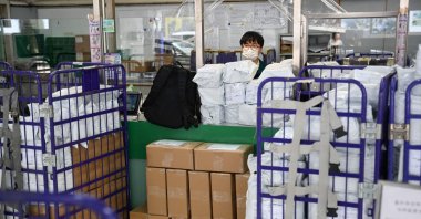 Stacked parcels are seen up front as a Hongkong Post employee stands at a service counter at a post office, Hong Kong, China, April 16, 2025. (AFP Photo)