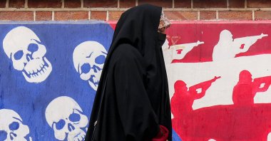 A woman walks past a mural depicting the U.S. flag with the stars substituted with skulls and the white and red stripes with silhouettes of soldiers firing assault rifles, painted on the outer walls of the former U.S. Embassy, Tehran, Iran, April 8, 2025. (AFP Photo)
