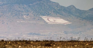 A flag of the Turkish Republic of Northern Cyprus (TRNC) and the motto of Mustafa Kemal Atatürk, &quot;Ne mutlu Türküm diyene&quot; (&quot;Happy is he who calls himself a Turk&quot;), seen on the slopes of the Beşparmak Mountains overlooking Nicosia (Lefkoşa), Turkish Cyprus, Aug. 10, 2024. (Reuters Photo)