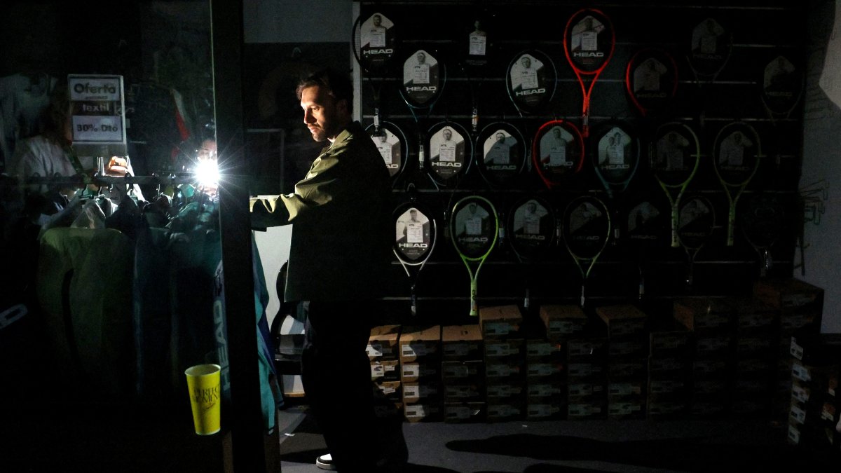 A man uses his cell phone&#039;s flashlight in a dark sports shop after the Madrid Open matches get suspended due to a power outage at the Park Manzanares, Madrid, Spain, April 28, 2025. (Reuters Photo)