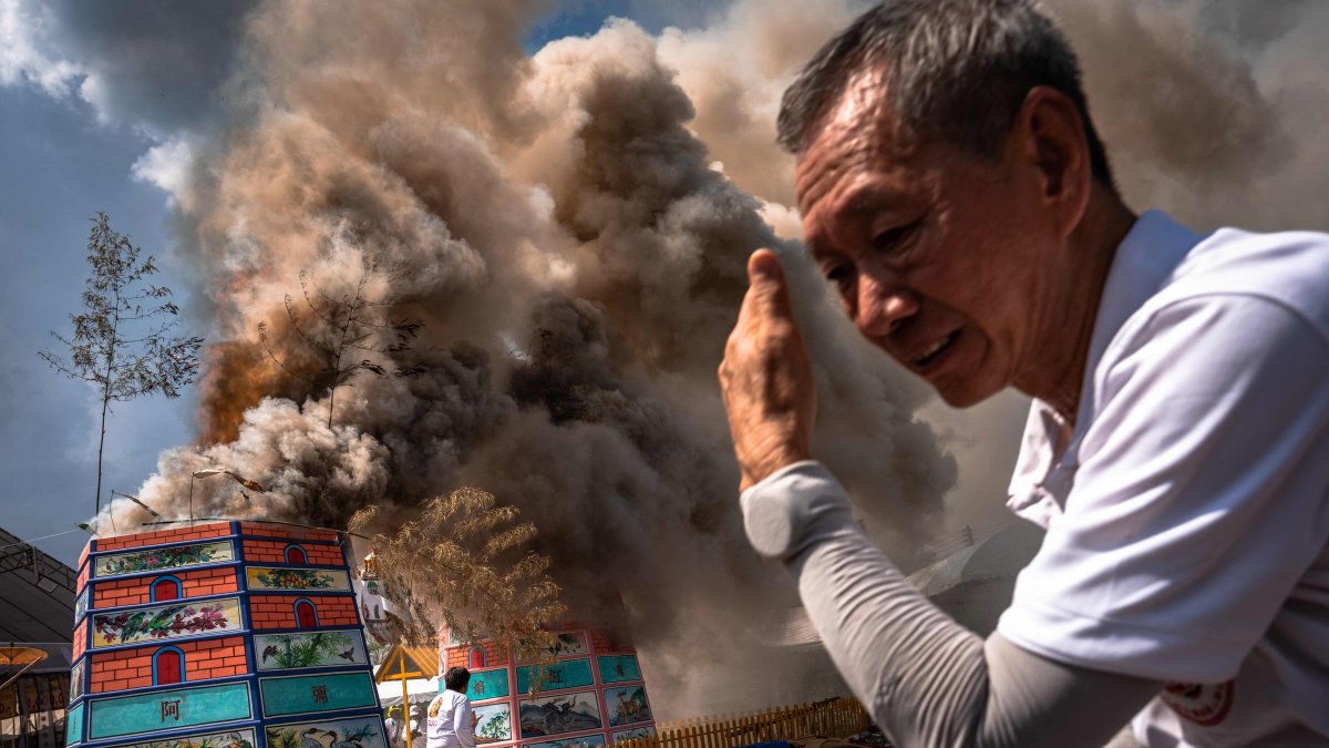 A volunteer shields himself from heat as smoke rises from cremations during the Lang Pacha ceremony at the Dhamma of Buddha Nakhon Ratchasima Foundation complex, Nakhon Ratchasima, Thailand, April 23, 2025. (AFP Photo)