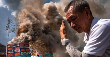 A volunteer shields himself from heat as smoke rises from cremations during the Lang Pacha ceremony at the Dhamma of Buddha Nakhon Ratchasima Foundation complex, Nakhon Ratchasima, Thailand, April 23, 2025. (AFP Photo)