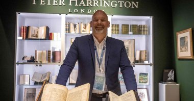 Pom Harrington, the owner of rare book dealers Peter Harrington, poses for a picture behind a mediaeval manuscript of Islamic Pharmacology by Ibn Sina, book five of his "Canon of Medicine," (L) and a 1798-99 rare first edition of the first Arabic dictionary printed in the Arab world, attributed to Jean-Joseph Marcel, Abu Dhabi International Book Fair, UAE, April 28, 2025. (AFP Photo)