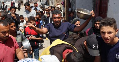A Palestinian man reacts as people queue to receive a food portion from a charity kitchen in the Bureij refugee camp in the central Gaza Strip on April 29, 2025. (AFP Photo)