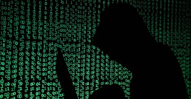 A hooded man holds a laptop computer as cyber code is projected on him in this illustration picture taken on May 13, 2017. (Reuters Photo)