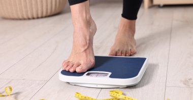 A woman stepping on a floor scale and using a measuring tape at home. (Shutterstock Photo)