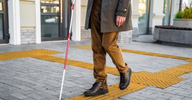 A blind man uses a walking stick to navigate the streets of the city, relying on tactile tiles for self-orientation. (Shutterstock Photo) 