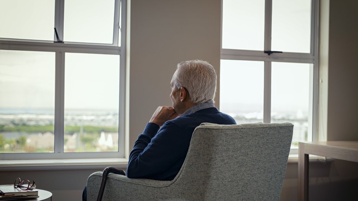 A man sits alone in his home, gazing out the window. (Shutterstock Photo)