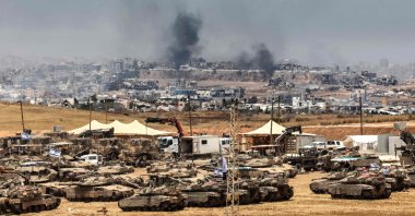 This picture taken from a position in southern Israel on the border with the Gaza Strip shows Israeli tanks and bulldozers deployed as smoke billows over destroyed buildings in Gaza during Israeli bombardment, May 17, 2025. (AFP Photo)
