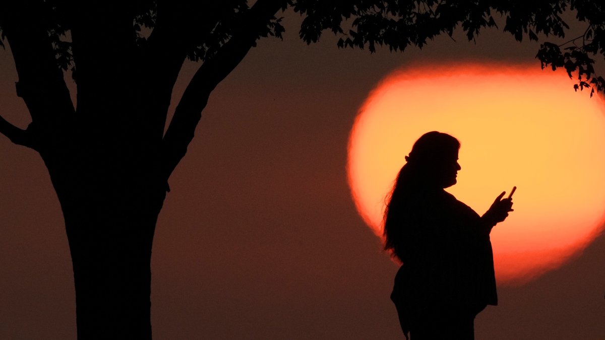 A woman looks at her phone while watching the sun set, Kansas City, U.S., Aug. 20, 2023. (AP Photo)