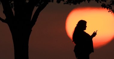 A woman looks at her phone while watching the sun set, Kansas City, U.S., Aug. 20, 2023. (AP Photo)