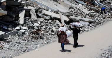 A Palestinian woman and a girl carrying bags of firewood walk by the rubble of houses, in Gaza City, Palestine, May 20, 2025. (Reuters Photo)