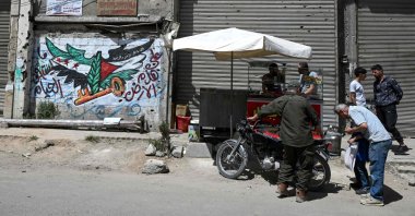 Men check a motorbike next to a mural painting bearing an image of the Syrian and Palestinian flags in the Yarmuk camp, Damascus, Syria, May 22, 2025. (AFP Photo)