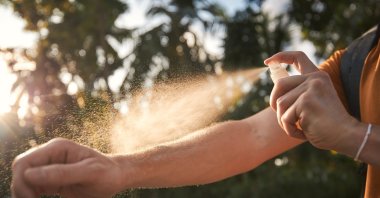A man applies insect repellent to his hands before entering the forest to protect against ticks and other insects. (Shutterstock Photo)