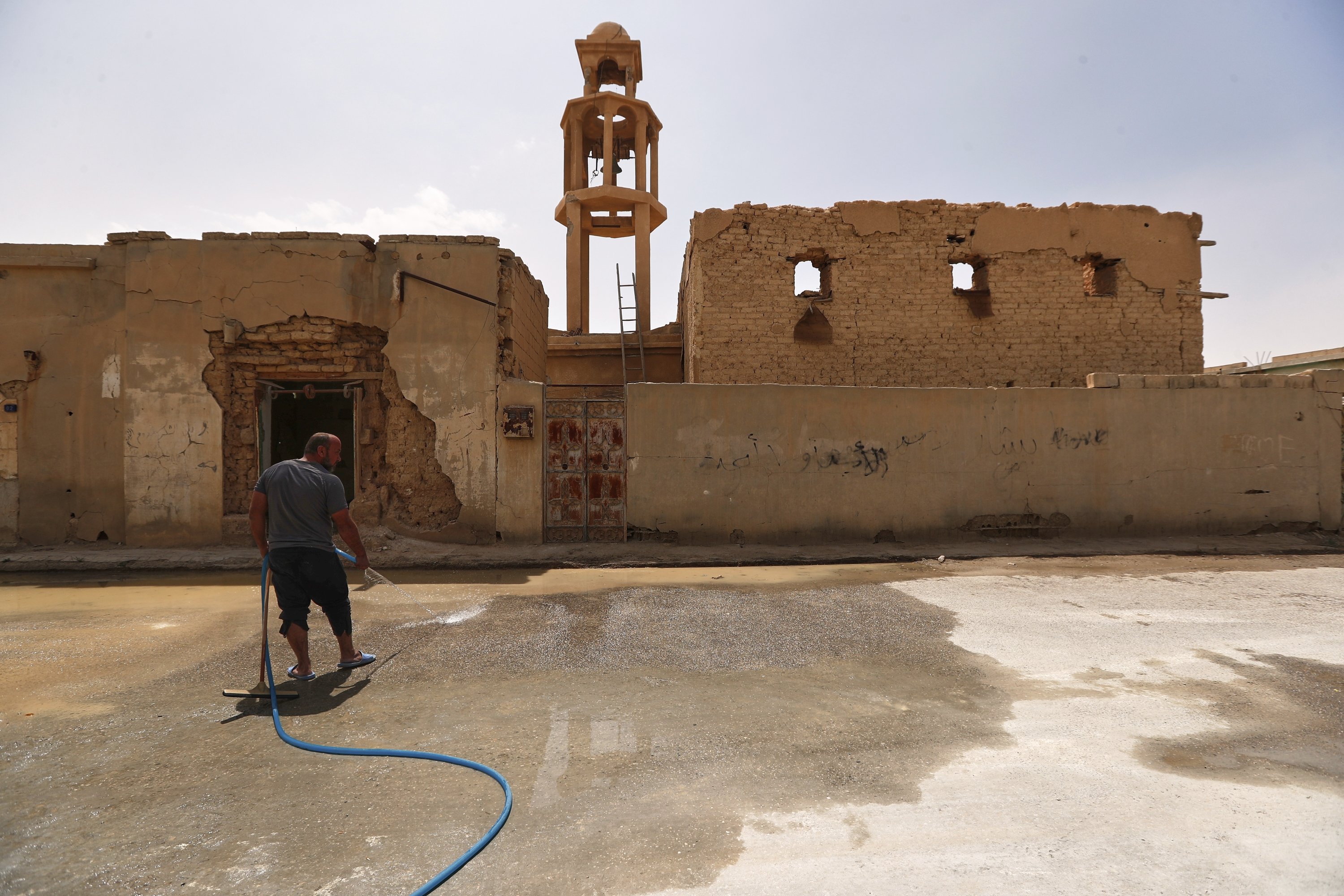 A man cleans the street beside a destroyed old church as families return to their homes after spending nine years in a notorious displacement camp in the Syrian desert, al-Qaryatayn, Syria, June 3, 2025. (AP Photo)